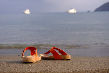 Slippers on the beach with ships on the background. Summer holiday concept.