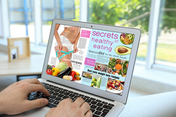 Man reading online magazine on laptop indoors, closeup