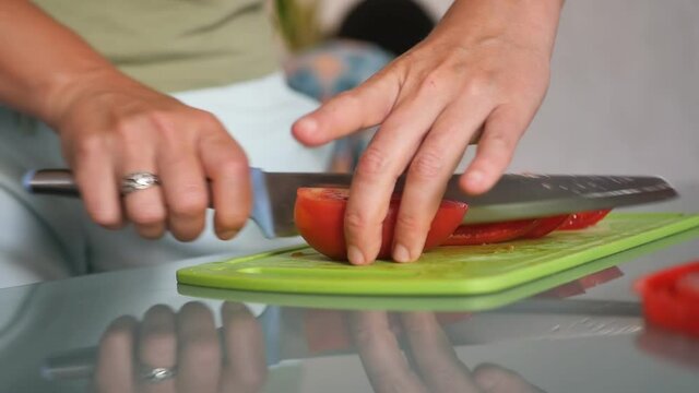 Close-up of a Caucasian woman with her hands holding a sharp knife and cutting into pieces red tomatoes on a green board. Slow motion. Healthy food. Vegetable salad