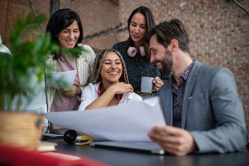 Fototapeta premium Cheerful young and old businesspeople sitting and working at desk in office, cooperation concept.