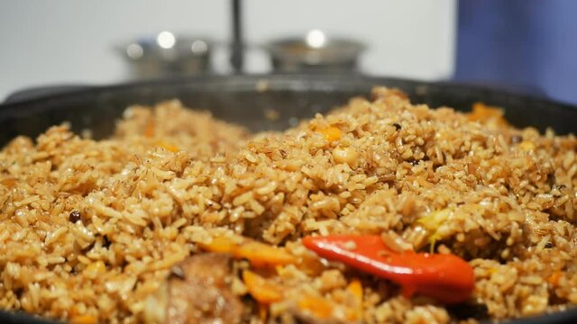 the cook's hand opens the lid of a large cauldron with cooked hot pilaf with lamb, carrots, cumin, onions, chickpeas, red and green peppers and brown rice. Close-up national uzbek food