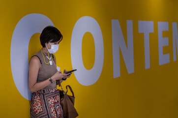 Side view of young asia woman wearing face mask and using a smart phone typing text message while...