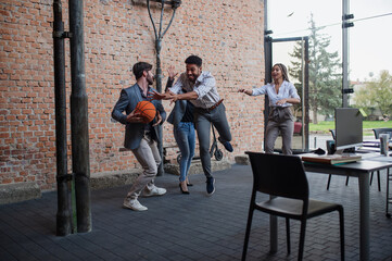 Group of cheerful young businesspeople playing basketball in office, taking a break concept.