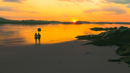 The silhouette of two people on the beach as the sun sets.