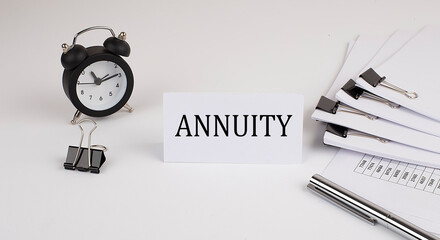 Card with text ANNUITY on a white background, near office supplies and alarm clock. Business concept.