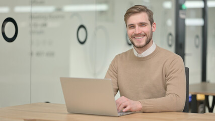 Young Man with Laptop Smiling at the Camera 