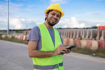 Asian construction worker holding a smartphone and smiling at the construction site