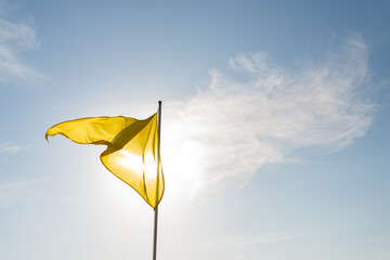 Yellow flag flapping in the wind and shadowing the sun,  San Sebastian, Spain. Blue sky with white clouds on the background.