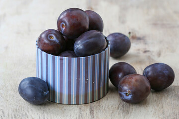 Bowl with ripe plums on wooden table