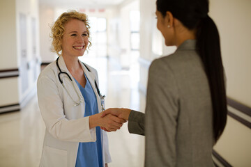 Doctor and businesswoman handshaking in hospital corridor