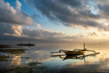 Fototapeta na wymiar Fishing boat at sunrise Bali coral beach, on the seascape background