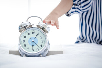 A young woman just woke up from her sleep when she heard the alarm clock at 6 in the morning. Put your hand on the button to mute the clock. concept of work, health care