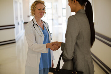 Obraz premium Doctor and businesswoman handshaking in hospital corridor
