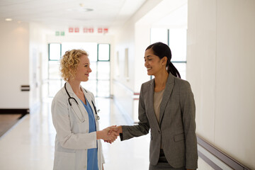 Doctor and businesswoman handshaking in hospital corridor