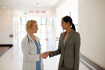 Doctor and businesswoman handshaking in hospital corridor