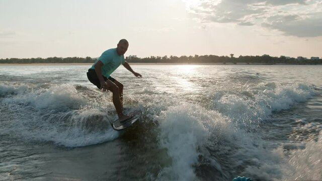 A surfer jumping on a wakeboard. An experienced wakeboarder sprays water drops into the camera.