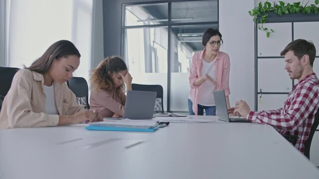 Angry female boss shouting at employees during business meeting, management