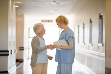 Fototapeta premium Nurse and senior patient shaking hands in hospital corridor