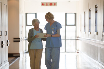 Nurse and aging patient reading chart in hospital corridor