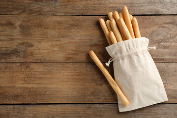 Delicious grissini sticks in bag on wooden table, flat lay. Space for text