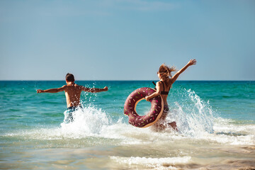 Happy young couple are having fun with inflatable donut at sea beach. Tropical vacations concept