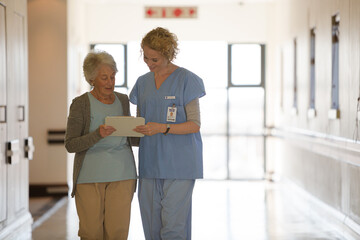Fototapeta premium Nurse and aging patient reading chart in hospital corridor