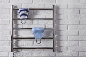 Modern heated towel rail with cloth face masks on white brick wall