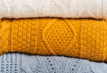 A stack of cozy knitted autumn-winter sweaters in yellow, white, blue colors. Cleaning and...