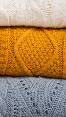 A stack of cozy knitted autumn-winter sweaters in yellow, white, blue colors. Cleaning and organization of space, clothes. Wardrobe