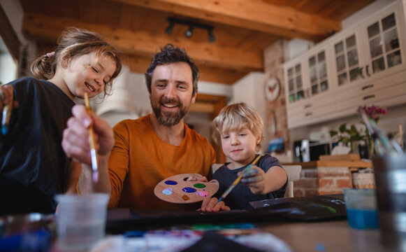 Mature father with two small children resting indoors at home, painting pictures.