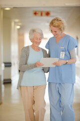 Nurse and aging patient reading chart in hospital corridor