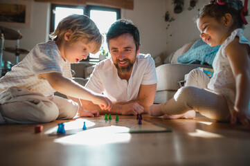 Mature father with two small children resting indoors at home, playing board games.