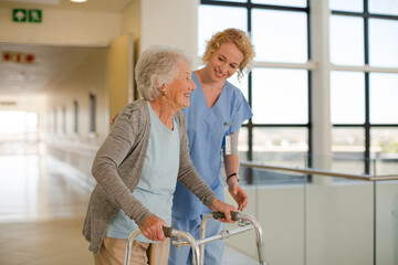 Nurse helping senior patient with walker in hospital corridor