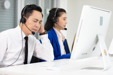 male operator wearing headphones, feeling tired and have a headache form overworked at call center service