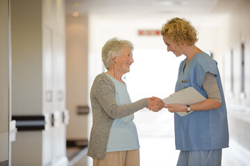Fototapeta premium Nurse and senior patient shaking hands in hospital corridor