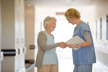 Fototapeta premium Nurse and senior patient shaking hands in hospital corridor