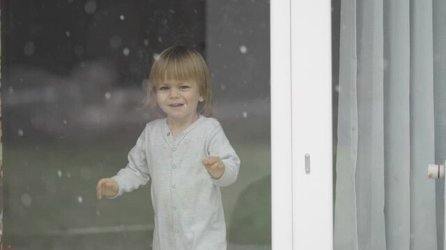 Portrait of funny little child stand at window and waving hand, winter, snowy