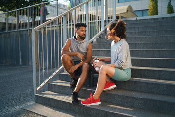 Fototapeta na wymiar Man and woman friends sitting on stairs outdoors in city, talking after exercise.