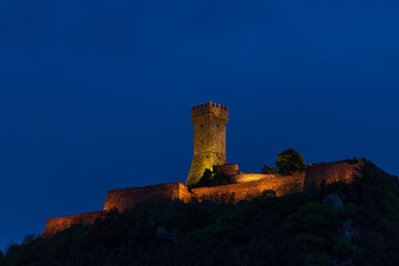 Obraz premium Radicofani, a medieval village and fortress in Tuscany, Italy. Unique view at dusk, the stone tower perched on rock cliff illuminated at dusk against blue sky.