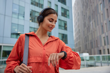 Female runner looks at smartwatch while going for run checks time listens music via headphones...
