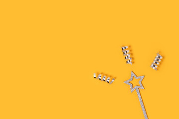 Glittering magic wand with silver colored confetti on a yellow background with copy space.