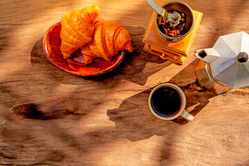 hot coffee in a white ceramic mug on an old wooden table, croissant in white plate, and coffee kettle
