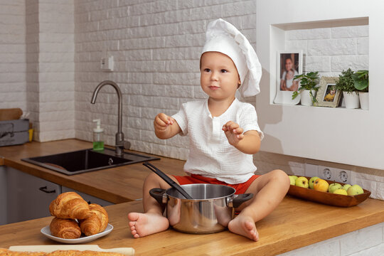 A Small Child In A Chef's Hat In The Kitchen Plays With A Saucepan, Joint Cooking With Children, Homemade Cakes, Family Recipes