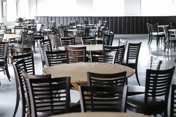 Empty ballroom, with several round tables, no decorations, and dark brown chairs. In the background...