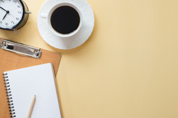 Office table with notepad, notebook, pencil, clock and coffee cup. Flat lay and top view with copy space.