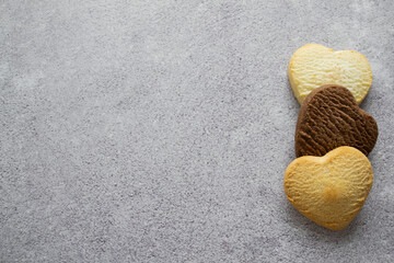Fototapeta na wymiar Three sweet heart-shaped cookies: vanilla, lemon, chocolate on the left. Gray background, copy space