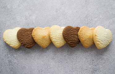 Fototapeta na wymiar Multicolored cookies in the shape of a heart: vanilla, lemon, chocolate. Gray background, copy space