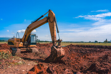 Backhoe or excavator working on land of countryside, excavator dig soil in rice field site industry, blue sky and green field agriculture background