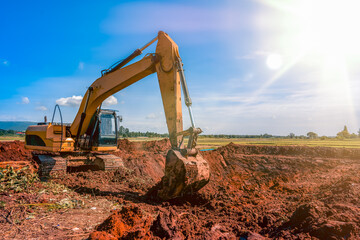 Fototapeta na wymiar Backhoe or excavator dig soil in rice field site industry, excavator on land on blue sky and green field agriculture background