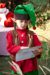 cute girl elf reads letters from children in a suit holding a white envelope and a sheet for Christmas and New Year